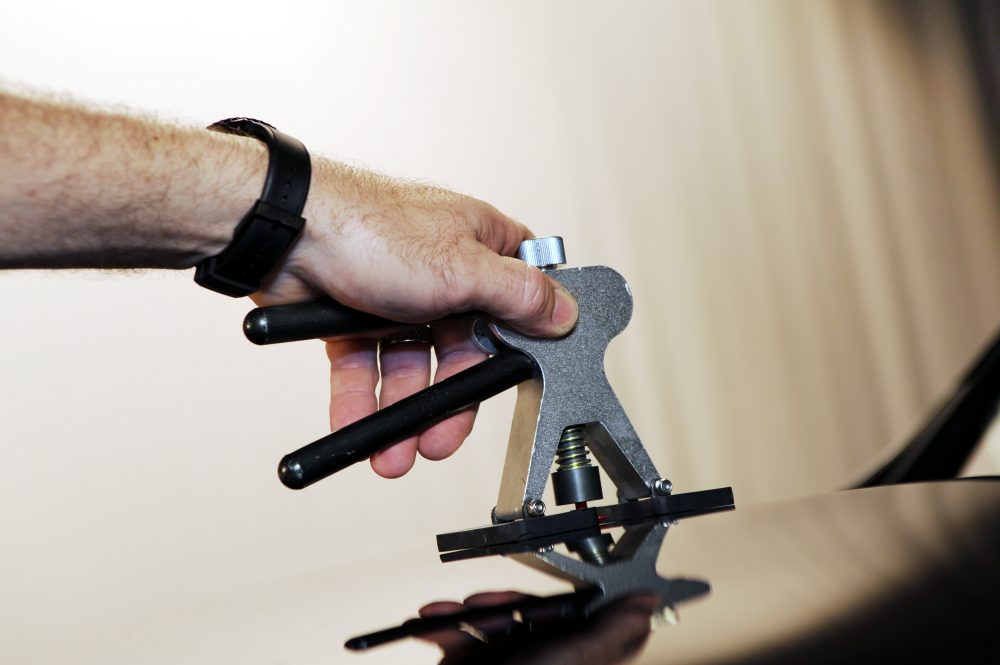 A hand holds a specialized dent-repair tool against a vehicle serface